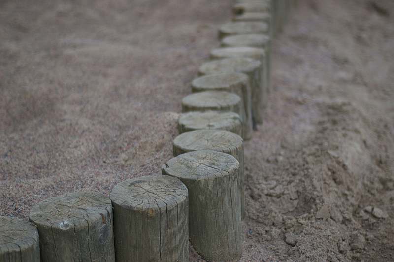 Close-up of hands installing black metal garden edging along a flower bed with trowel and gloves